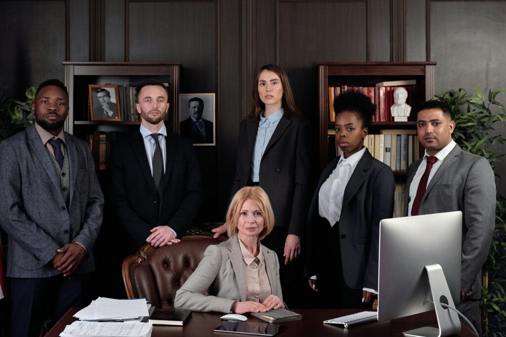 A confident businesswoman seated at a desk with her diverse team standing behind her.