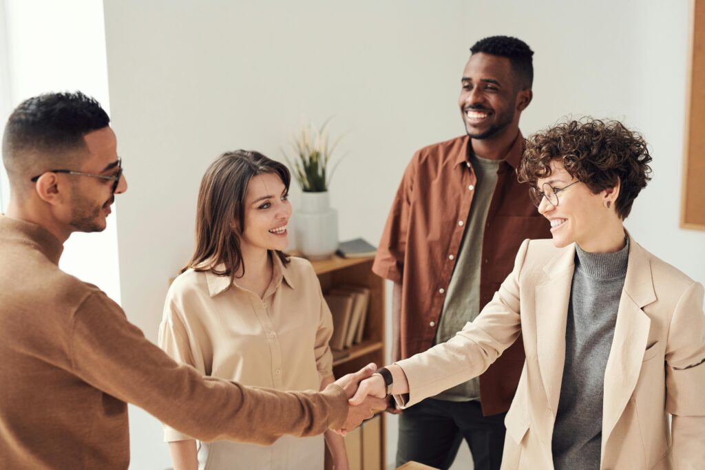 Four diverse colleagues shaking hands and smiling in a bright office.