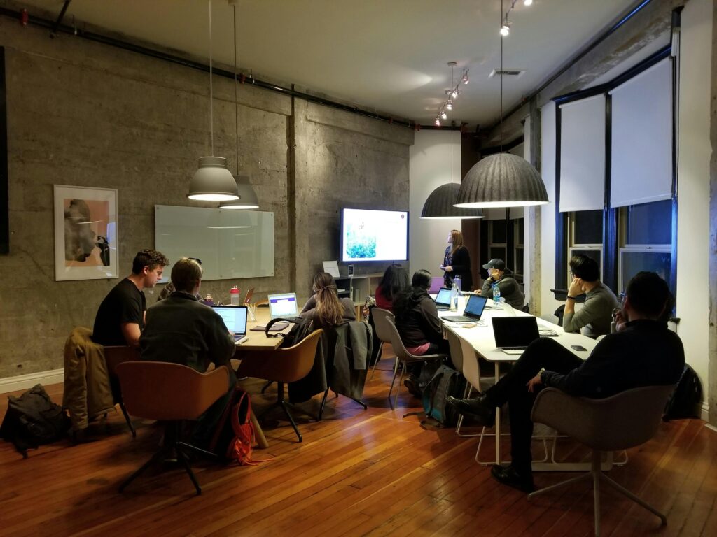 A group of people in a modern meeting room with laptops and a presentation screen.